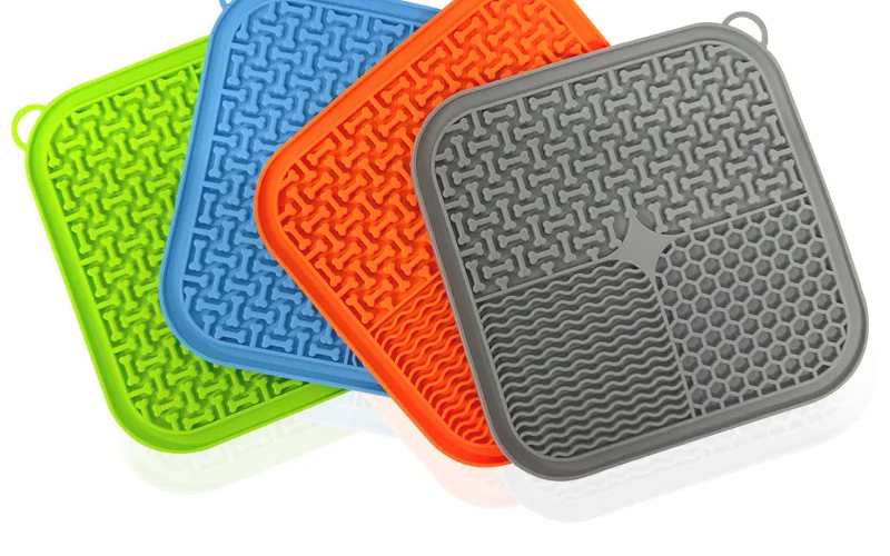 The silicone lick mat in the four colourways the manufacturer makes (green, blue, orange and grey), fanned out on a white background. The mat sold here is the green one.