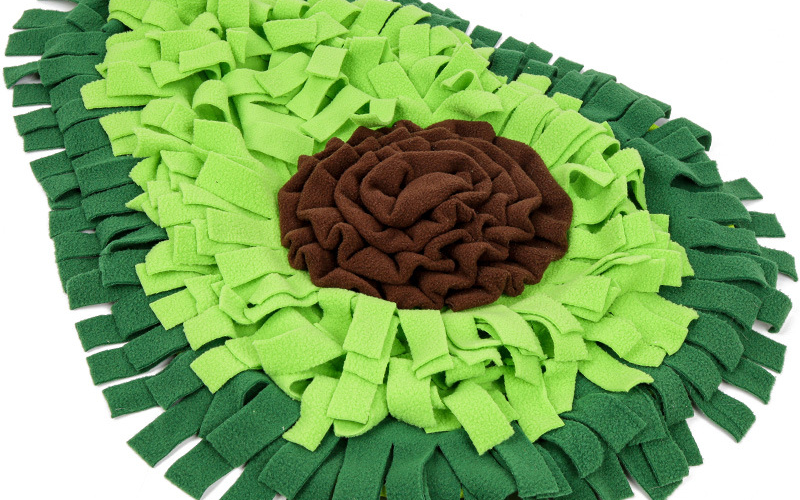 The green avocado-shaped snuffle mat seen from above: two-tone green fleece strips around a brown fleece rosette, on a white background.