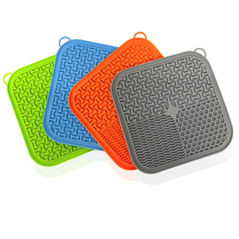 The silicone lick mat in the four colourways the manufacturer makes (green, blue, orange and grey), fanned out on a white background. The mat sold here is the green one.