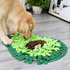 The green avocado snuffle mat in use on a wooden floor at home, a dog searching it beside a houseplant.